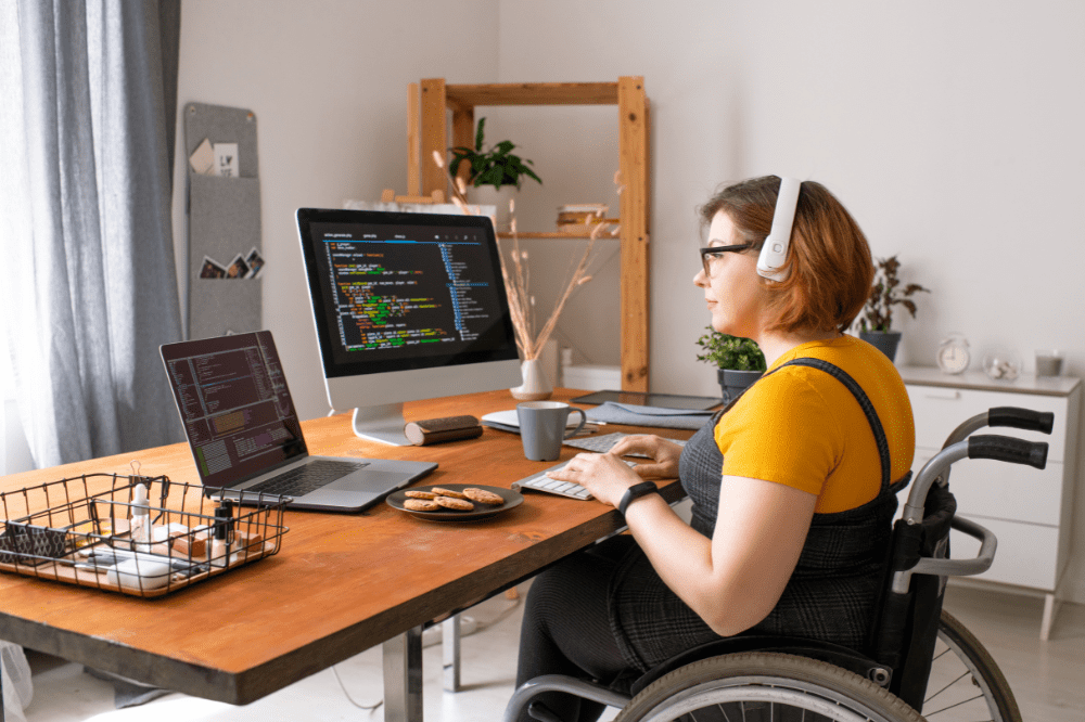 Home Based Businesses for Disabled. A woman in a wheelchair at a desk with a computer. She has headphones on.