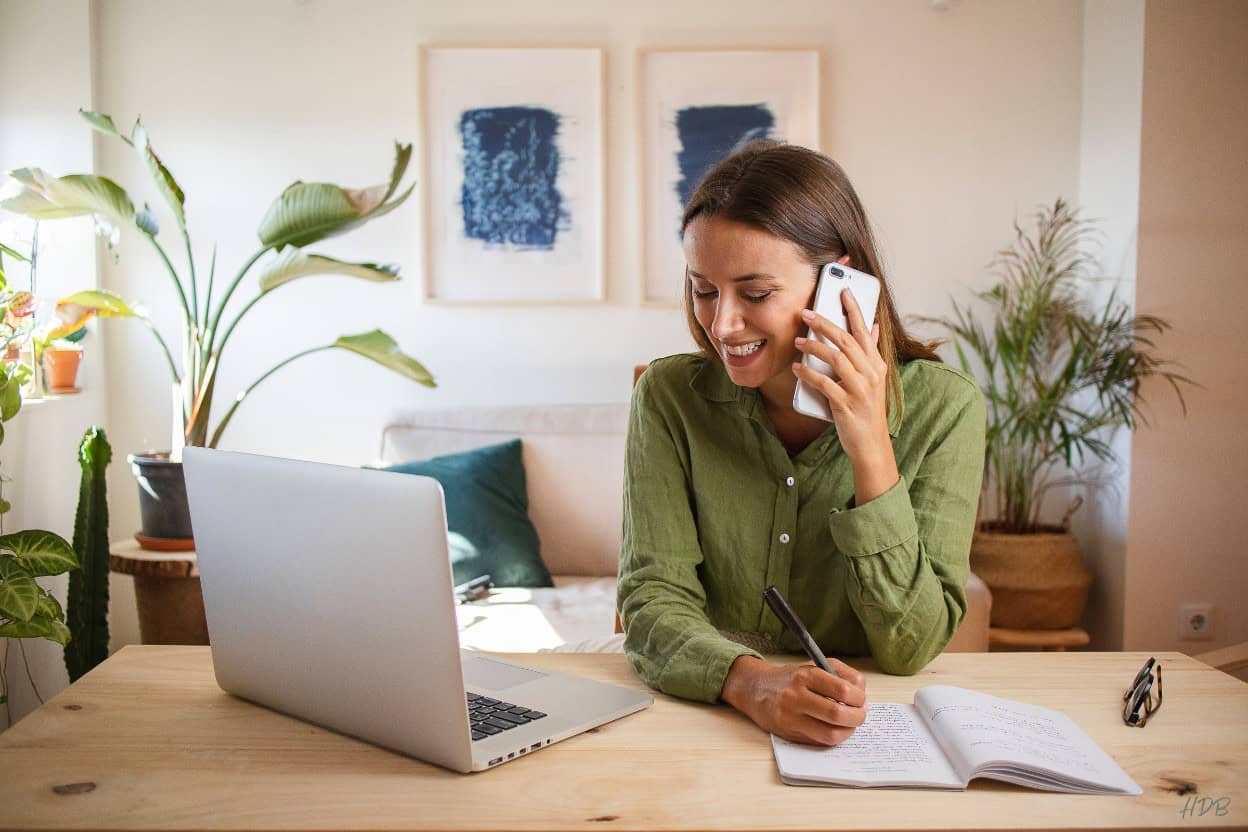 woman at desk on cell phone with laptop